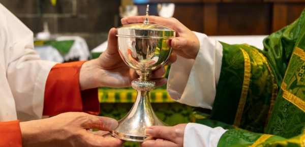 Close-up: priest’s hands giving ciborium (covered cup holding Communion host) to server.