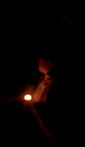 A person with a candlelight against a very dark background.
